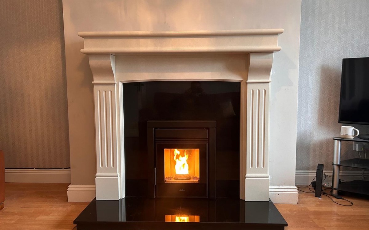 A cream limestone fireplace surround with a stove lit, fitted by Stove Fit
